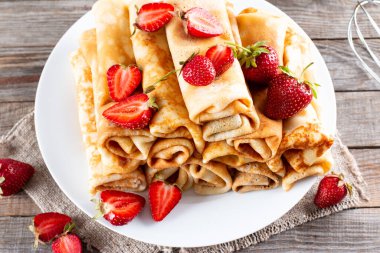 Çilekli bir sürü krep. Maslenitsa. Ahşap arka planda çilekli taze pişmiş krep yığını..