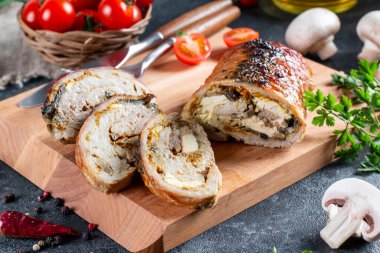 Mantarla doldurulmuş domuz eti ruloları ve ahşap bir tahtanın üzerinde sebzelerle servis edilen peynir.