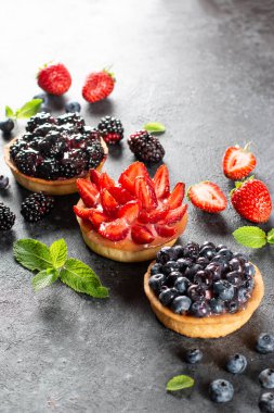 Gri arka planda kremalı meyveli tartlar. Yaz meyveli kek. Çilekli tart, yaban mersini, böğürtlen. Seçici odak