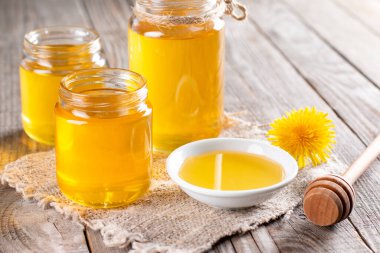 Flower honey in a glass jar and dandelions on a wooden table clipart