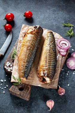 Baharatlı, biberli ve sebzeli füme balığı kara taş arka planda el işi kağıdında görmek. Akdeniz yemeği, ringa balığı, deniz ürünleri, üst manzara.