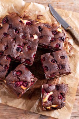 Chocolate brownie with cherries and cheese layer. Many pieces of chocolate dessert with berries on a wooden board