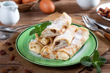 Thin pancakes with cottage cheese and raisins on rustic wooden table. Healthy traditional breakfast concept.