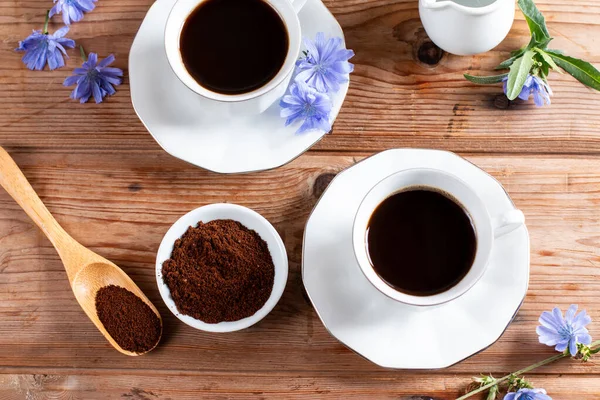 Healthy hot chicory drink in the cup , crushed chicory root in small white bowl and milk in glass jug on a wooden table. Top view