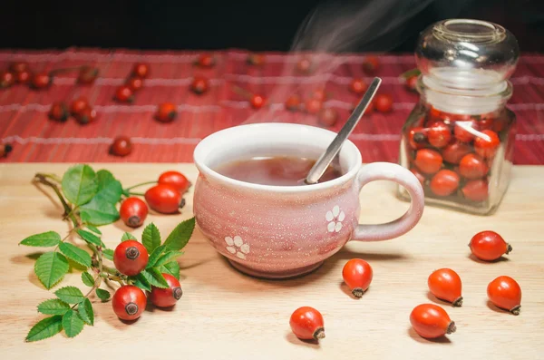 Bodegón con taza de té fresco y rosa mosqueta en la mesa de madera —  Fotos de Stock
