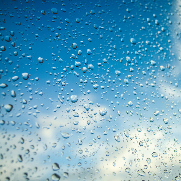 Капли воды на оконном стекле с голубым небом
