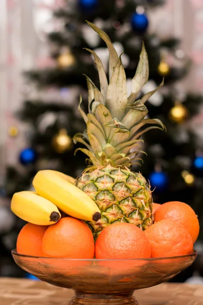 Plato con mandarinas, plátanos y piña en el fondo del árbol de Navidad —  Fotos de Stock