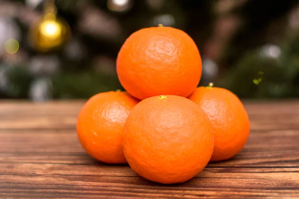 Nieuwjaar en Kerstmis. Tropisch fruit op een houten tafel. Tangerines op een houten achtergrond tegenover de kerstboom. — Stockfoto