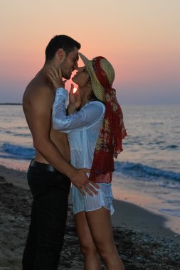 mutlu şefkatle kucaklayan ve gün batımında sahilde öpüşme genç Çift.