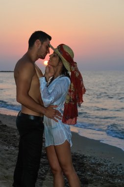 mutlu şefkatle kucaklayan ve gün batımında sahilde öpüşme genç Çift.