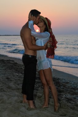 mutlu şefkatle kucaklayan ve gün batımında sahilde öpüşme genç Çift.
