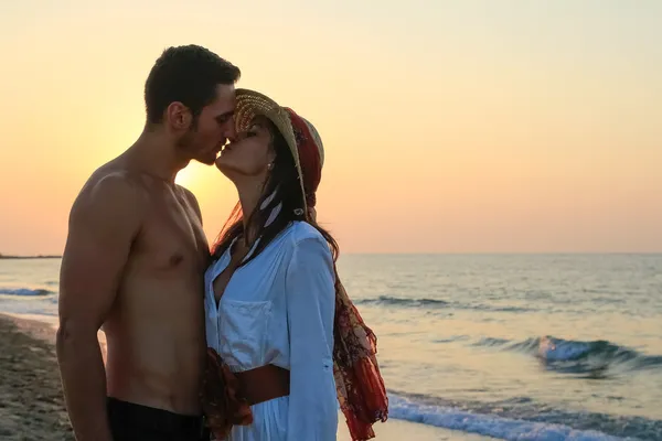 Felice giovane coppia teneramente abbracciare e baciare in spiaggia al tramonto . — Foto Stock