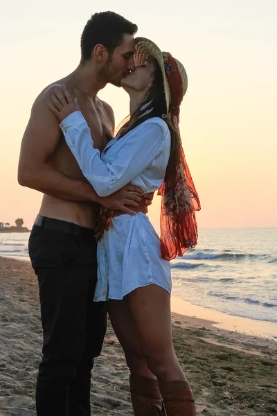 Feliz joven pareja tiernamente abrazando y besándose en la playa al atardecer . —  Fotos de Stock