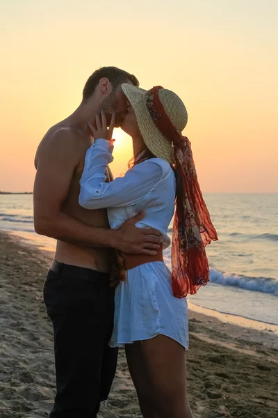 Feliz jovem casal ternamente abraçando e beijando na praia ao entardecer . — Fotografia de Stock