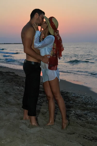 Glückliches junges Paar, das sich in der Abenddämmerung am Strand zärtlich umarmt und küsst. — Stockfoto