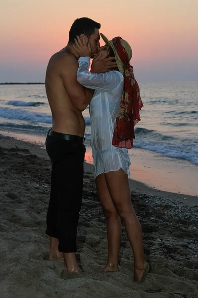 Feliz joven pareja tiernamente abrazando y besándose en la playa al atardecer . —  Fotos de Stock