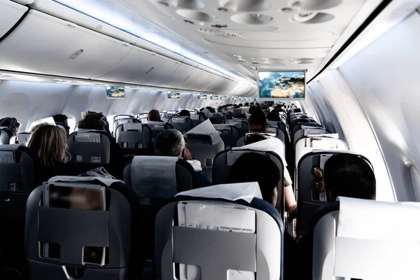 Passenger cabin of commercial aircraft with unrecohnizable travellers seated on their seats during flight. — Stock Photo, Image