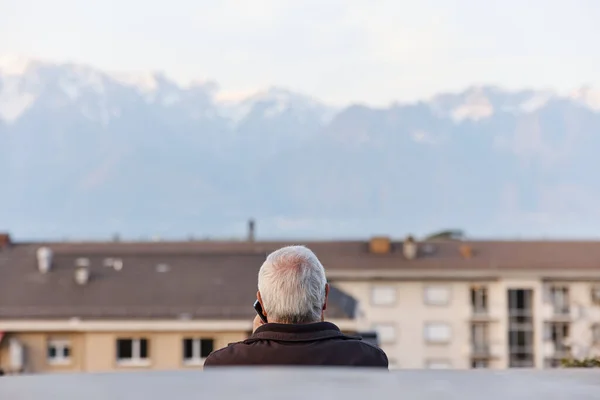 Pria senior berbicara di telepon di latar belakang Alpen di Swiss. Sudut belakang. Stok Foto