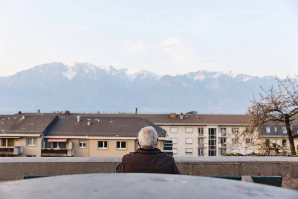 Idősebb férfi beszél telefonon az Alpok hátteréről Svájcban. Hátsó szög. Stock Fotó