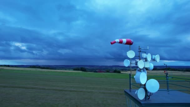 Chaussette de vent de l'aéroport rouge-blanc est soufflé par le vent contre un ciel orageux. Radars de communication radio sur le pont d'observation de l'aéroport. — Video