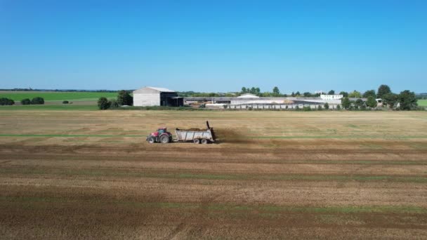 Concime organico. Un trattore con un diffusore per rimorchi diffonde sterco di mucca in un campo. Vista dal drone. — Video Stock