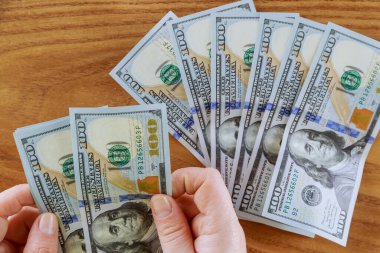 Elinde 100 dolarlık banknotlar, ahşap bir masada bir sürü para..