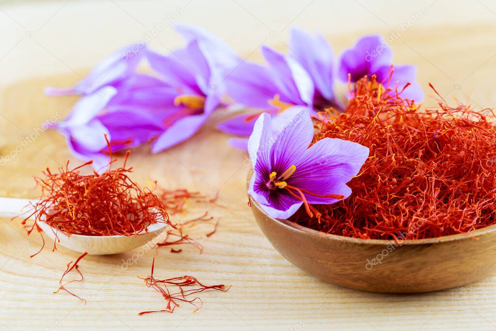 Dried saffron stamens and saffron flowers in a wooden plate and spoon on a wooden background. Stamens are used for cooking.