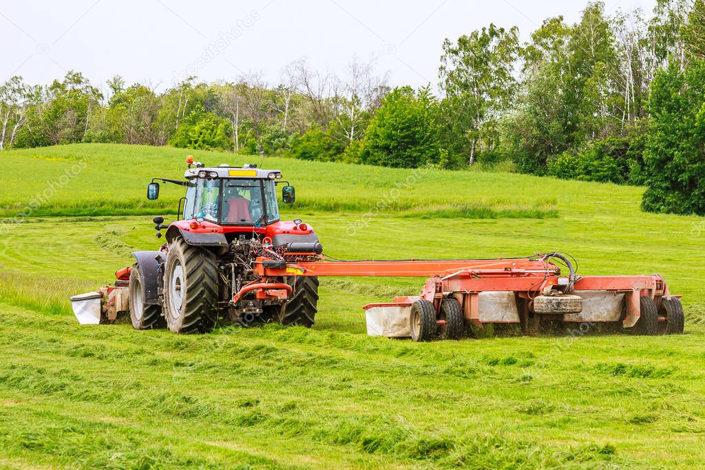 Tractor with a rotary mower mows the grass in the field.