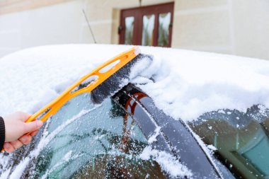 Karla kaplı bir araba. Eli olan bir adam özel fırçalarla arabanın ön camını kardan temizler. Soğuk hava..