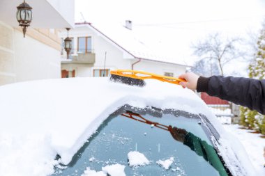 Karla kaplı bir araba. Bir adam özel fırçalarla arabayı kardan temizler. Soğuk hava..