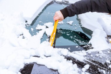 Karla kaplı bir araba. Bir adam özel fırçalarla arabayı kardan temizler. Soğuk hava..