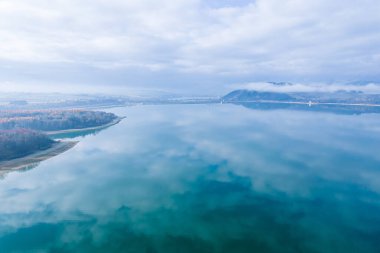 Yağmurdan sonra dağlarda yoğun sis var. Mavi gökyüzünün yansıması ve göldeki beyaz bulutlar.