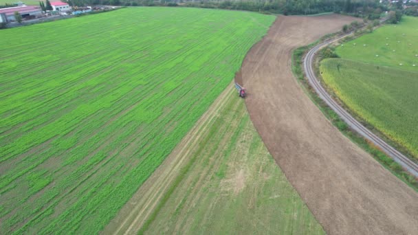 Das Feld wird in der Nähe der Bahn von einem Traktor gepflügt. Auf einem Feld in der Nähe des Dorfes wurde Gründünger ausgesät. Blick von oben. — Stockvideo