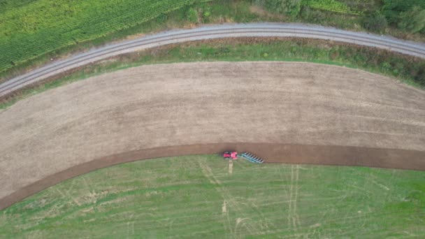 En röd traktor plogar ett fält vid järnvägen. Utsikt uppifrån. Grön gödsel växer på fältet. — Stockvideo