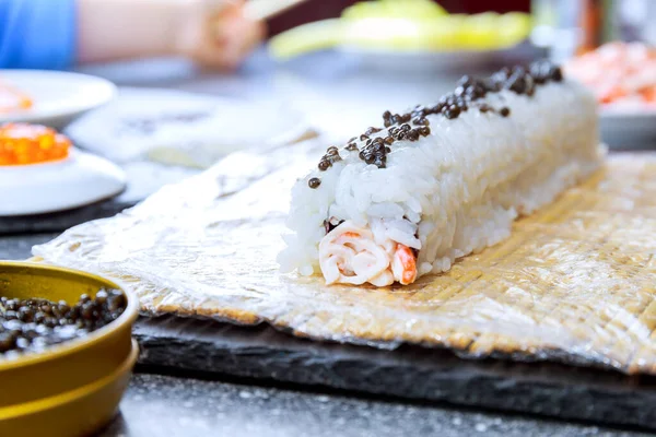 A sushi roll sprinkled with black caviar stands on a bamboo mat — Stock Photo, Image