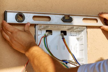 Elektrikçi, elektrik santralindeki voltaj kutusunu bir seviye kullanarak duvardaki deliğe yerleştirir..