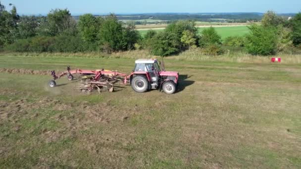A tractor with a rotary rake rakes hay on agricultural land. Aerial video recording by drone. — Vídeo de Stock