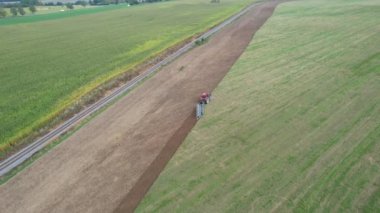Kırmızı traktörlü bir dronun videosu demiryolunun yakınına yeşil gübre ekilmiş bir tarlayı sürüyor..