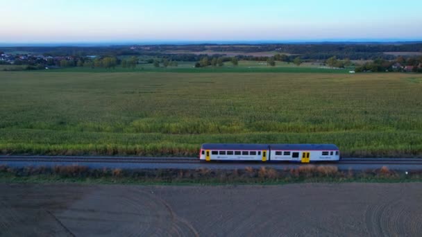 Un treno passeggeri viaggia per ferrovia tra campi agricoli. Vista dall'alto dal drone verso il lato del treno. — Video Stock