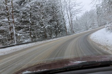 Kardan sonra ıslak bir yolda arabanın ön camından bak. Karla kaplı ağaçlar ve yol kenarları.