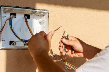 Elektrikçi elinde elektrikli tel ve kerpeten tutuyor. Bir elektrikçi elektrik panelini bağlamak için bir elektrik kablosunu tamir eder.