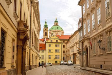8 Nisan 2019 Prag, Çek Cumhuriyeti: Uzun mimari binalar ve dar bir cadde. Kilise kubbesi ve saati olan bir bina..