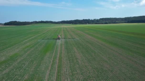 The tractor drives across the field, spraying fertilizer on a large field next to the forest. Top view. — Stock Video