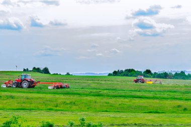 Two red tractors mow the grass in a farmer's field. Tractors mow a large area of agriculture.