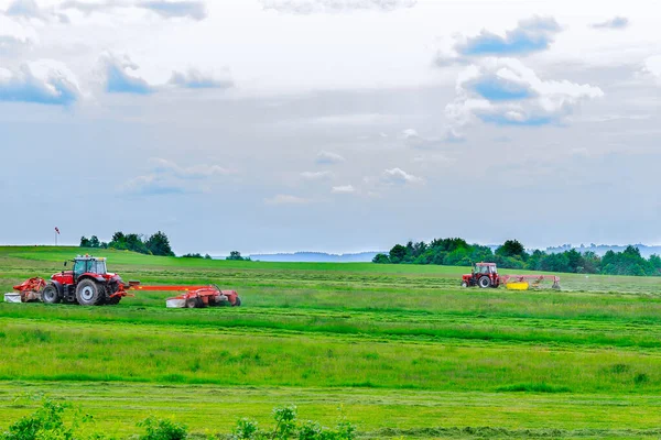 Two red tractors mow the grass in a farmer\'s field. Tractors mow a large area of agriculture.
