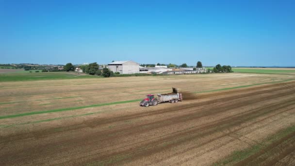 Трактор посыпает навозом поле рядом с фермой. Сельской местности. Удобрение почвы перед вспашкой. — стоковое видео
