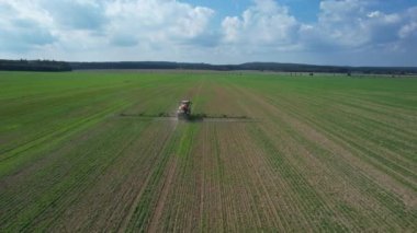 Bir traktör tarladan geçer, arabaların gittiği yolun yanındaki geniş bir tarlaya gübre püskürtür. Kırsal bölge. Yukarıdan bak. Modern ekipmanlar sahada çalışıyor..