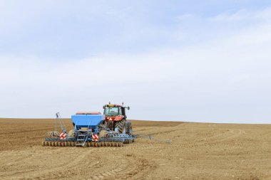 Mavi ekipmanlı kırmızı bir traktör, hassas çiftçilik için GPS navigasyonunu kullanarak bir tarlaya tahıl eker. Tarım sektörü.