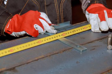 worker measures markings on a metal surface for drilling holes. The worker measures the required distance on the iron surface using a meter.