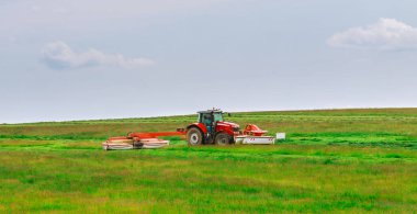 A red tractor mows the grass on a farmer's field. Two mowers will mow a large area of the field. Agricultural.
